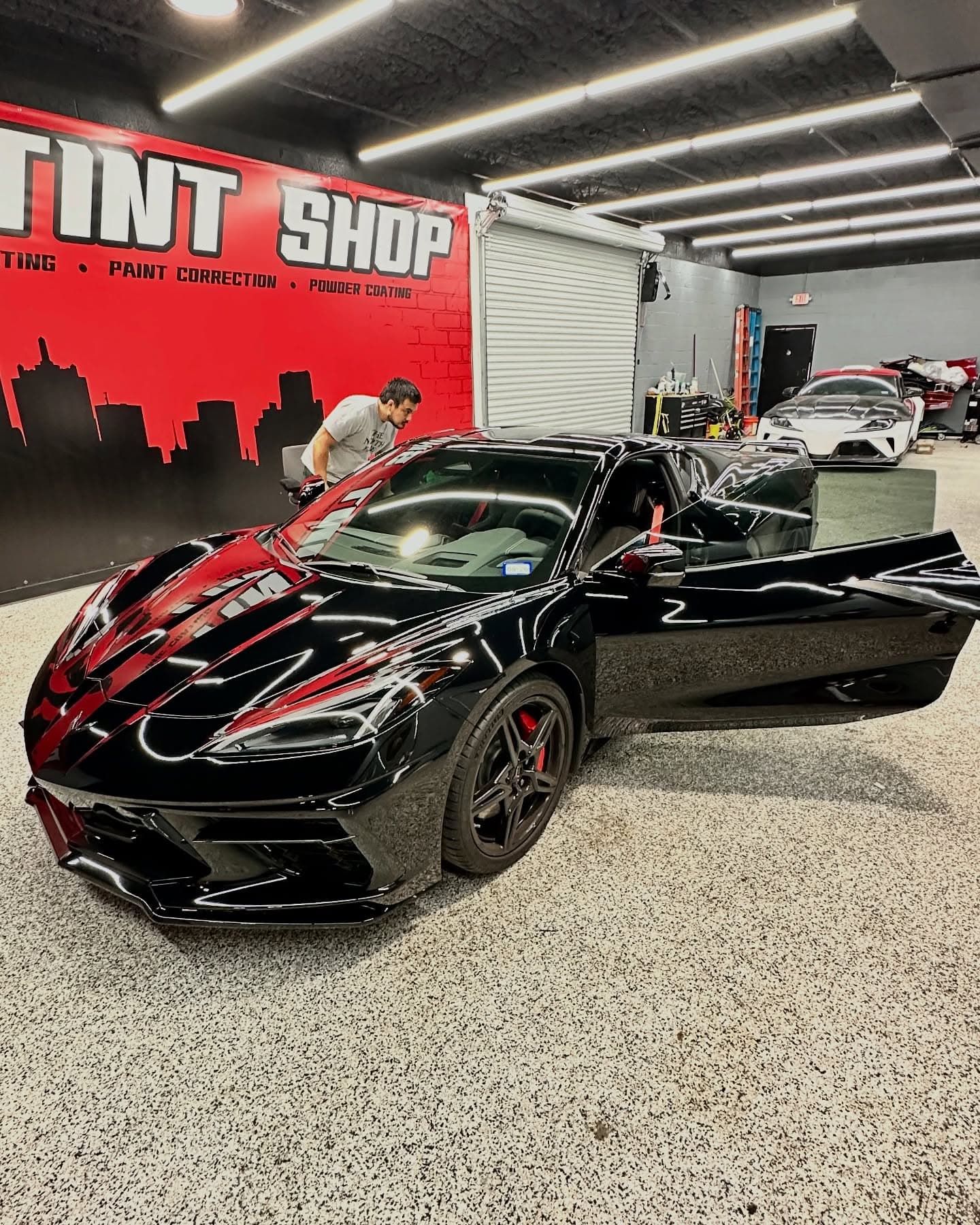 Black Corvette C8 in the bay against the Dallas Tint Shop mural